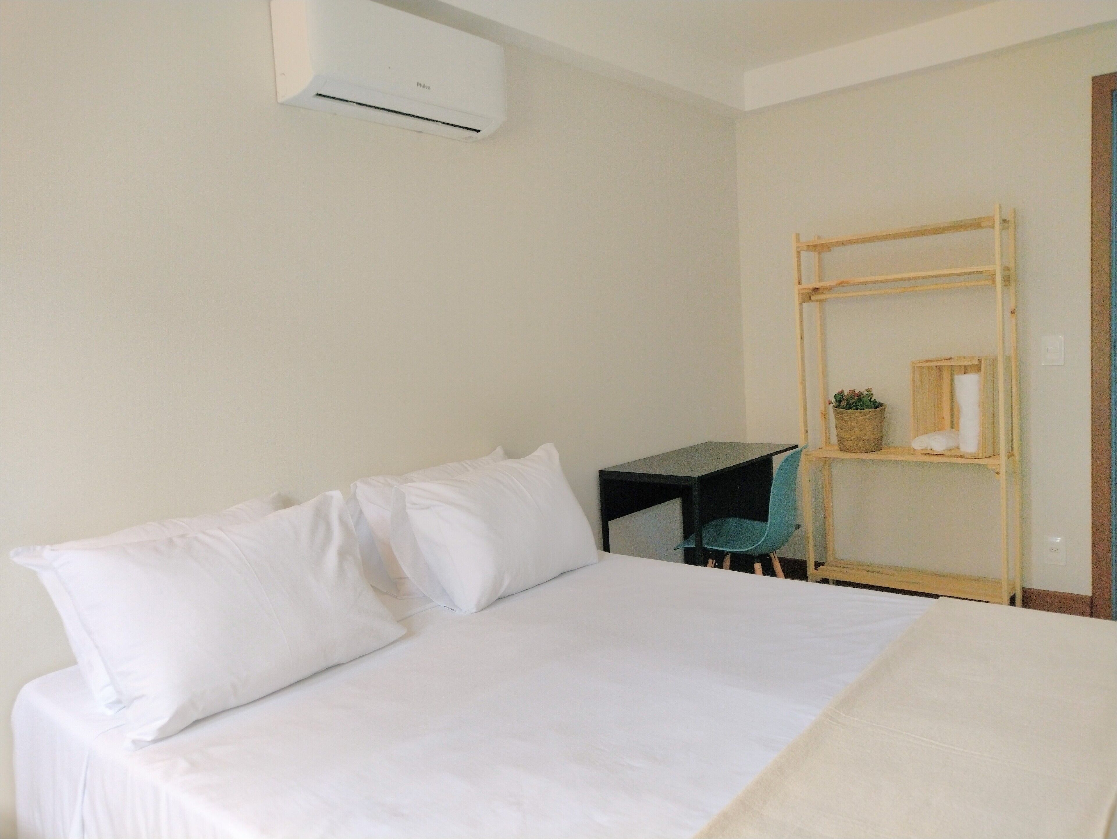 Una camera da letto con un letto, una scrivania, una sedia e uno scaffale con asciugamani e una pianta.