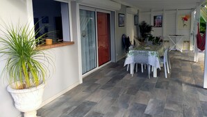 Un patio techado al aire libre con una mesa y sillas, una planta en maceta y una puerta corredera de vidrio.