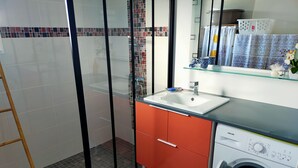Un baño moderno con cabina de ducha de vidrio, lavabo con encimera de cristal y lavadora de carga frontal.