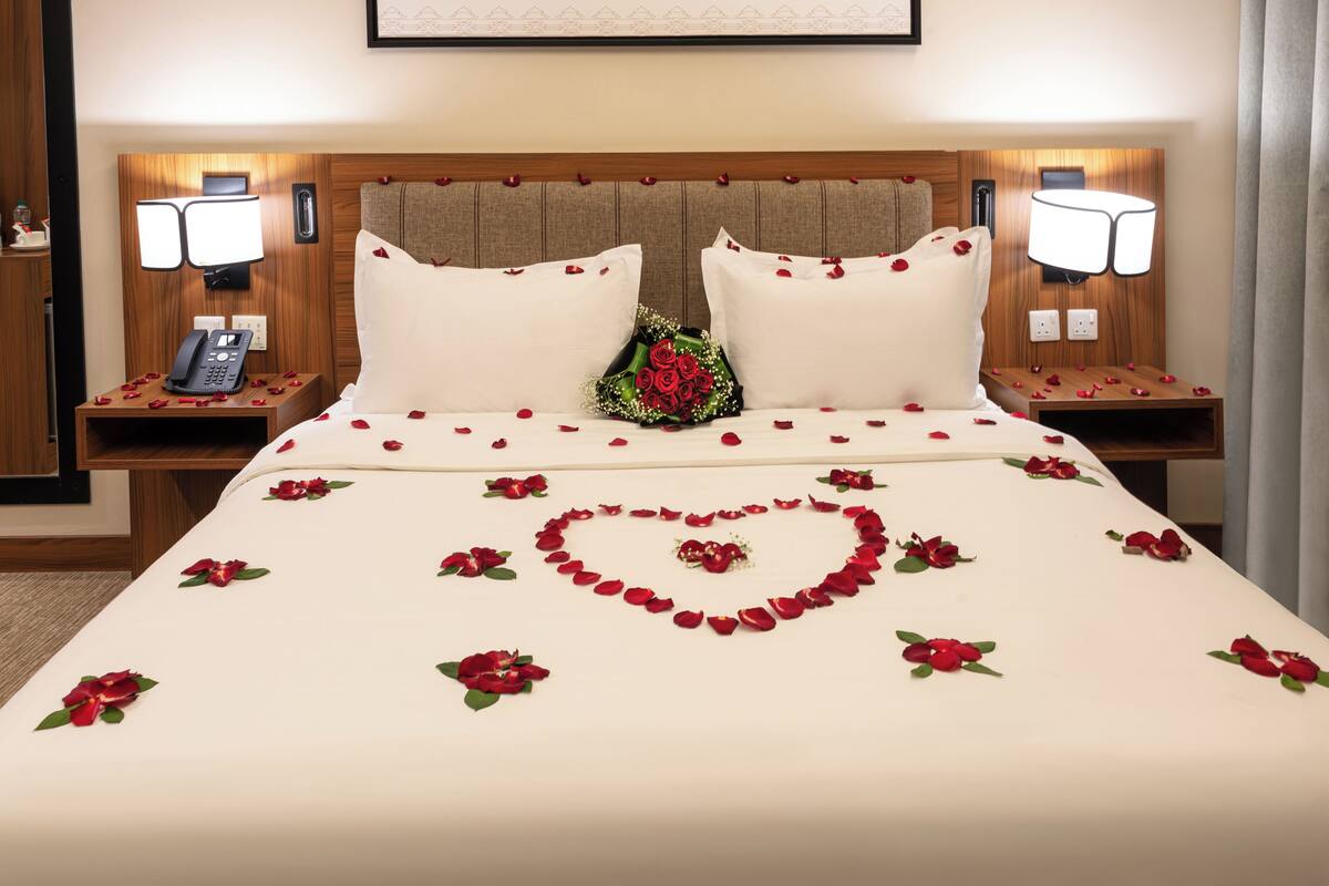 A hotel room with a large bed, two bedside tables, a nightstand, a wall-mounted telephone, and a framed picture above the bed.