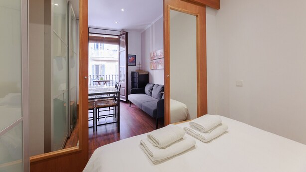 Ein Hotelzimmer mit einem Bett, einem Tisch und einem Stuhl. Es gibt einen Balkon mit Blick auf Gebäude.