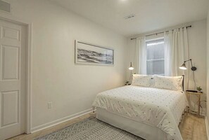 Een slaapkamer met een bed, een raam met gordijnen, een aan de muur hangend schilderij en twee bedlampen.