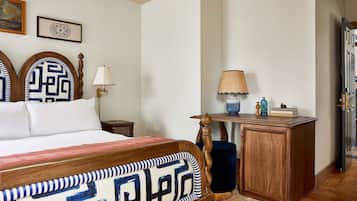 Un dormitorio con cama, cabecera de madera, mesita de noche, lámpara, cómoda y puerta.