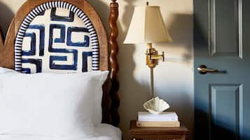 A neatly made bed with a patterned headboard, a bedside lamp, a framed picture above the bed, and a closed door.