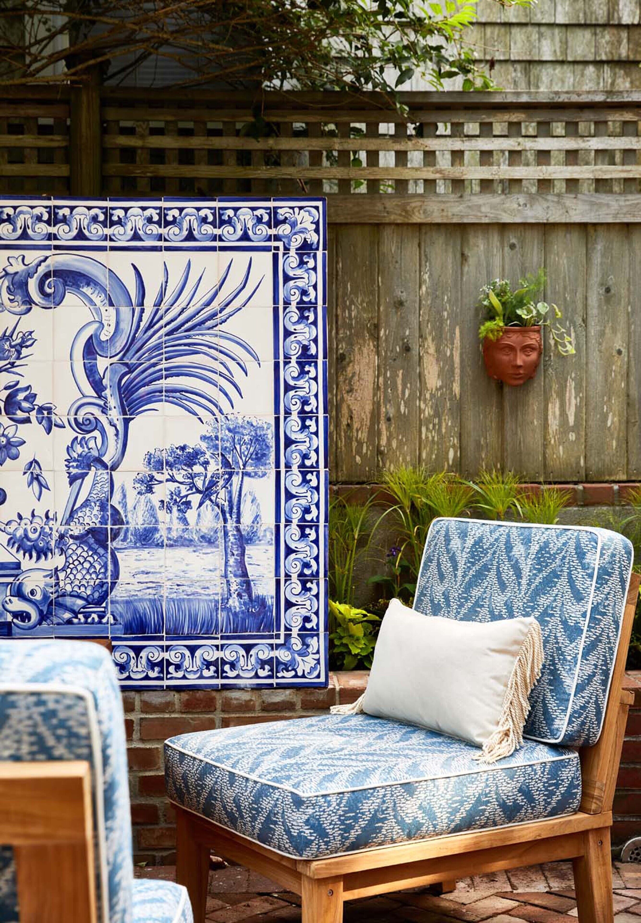 Uma área de pátio com uma cadeira de padrão azul e branco, um azulejo decorativo com o desenho de um dragão e uma cerca de madeira ao fundo.