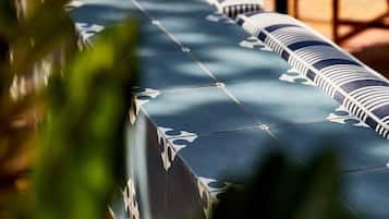 A long table covered with a patterned tablecloth, surrounded by chairs and tables in an outdoor setting.