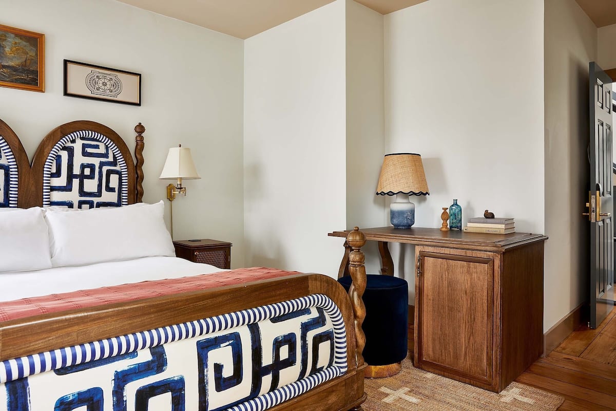 A bedroom with a bed, bedside tables, a desk with a lamp, and a door.