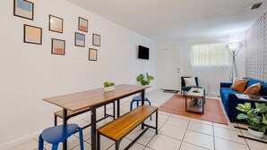 Una sala de estar moderna con una mesa de comedor de madera, sillas azules, un sofá azul y un televisor montado en la pared.