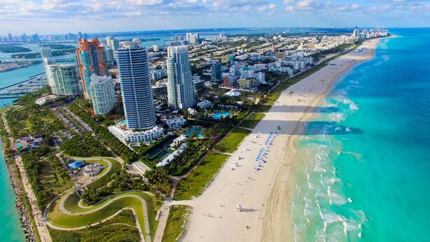 Vista aérea de una ciudad costera con rascacielos, una extensa playa y un puerto deportivo.
