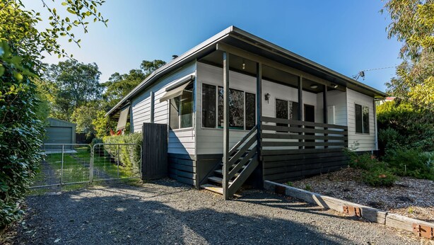 Une maison mobile de plain-pied dotée d’un porche couvert, d’une cour clôturée et d’une allée en gravier.