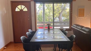Un coin repas avec une table et des chaises, une fenêtre donnant sur les arbres, une porte avec un panneau de verre et un mur orné d’une citation encadrée.