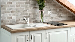 Una cocina con pared de ladrillo, armarios blancos, encimera de madera, un lavamanos y un florero con flores.