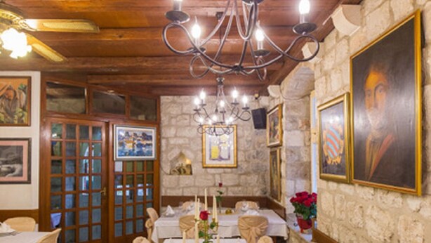 Una larga mesa de comedor con manteles blancos, velas y copas, rodeada de sillas color beige en una habitación con vigas de madera y paredes de piedra.