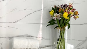 A bathroom with a marble wall, a glass vase with flowers, and a stack of white towels. - Rooms Sorgo Palace - Comfort Double Room (Ston)
