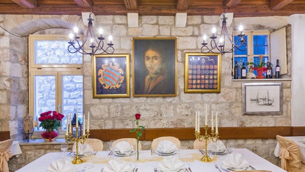 A dining room with a stone wall, chandeliers, framed artwork, and a table set for a meal. - Rooms Sorgo Palace - Comfort Double Room (Ston)