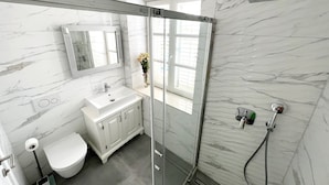 Een moderne badkamer met een douchecabine van glas, een witte wastafel en een toilet.