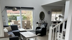 Ein modernes Wohnzimmer mit Sofa, Couchtisch und Sesseln, ein Essbereich mit Tisch und Stühlen sowie eine Treppe, die zu einer weiteren Ebene führt.