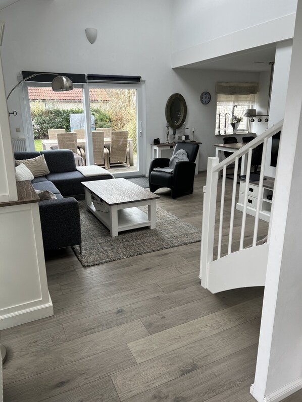 A modern living room with a sofa, coffee table, and chairs, a dining area with a table and chairs, and a staircase leading to another level.