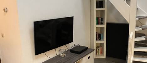 Una sala moderna con un televisor de pantalla plana montado en una pared blanca, un mueble bajo para equipo multimedia de madera y una escalera que conduce a un piso superior.