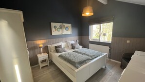 Ein Schlafzimmer mit einem weißen Bett, einem Nachttisch mit Lampe, einem Fenster mit Aussicht und einer Heizung.