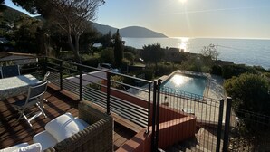 Eine Terrasse mit Gartenmöbeln, ein Schwimmbad und Blick auf Meer und Berge.
