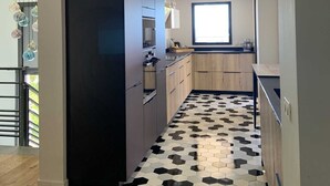 Eine moderne Küche mit einem schwarzen Kühlschrank, Holzschränken und einem Boden aus schwarz-weißen, sechseckigen Fliesen.