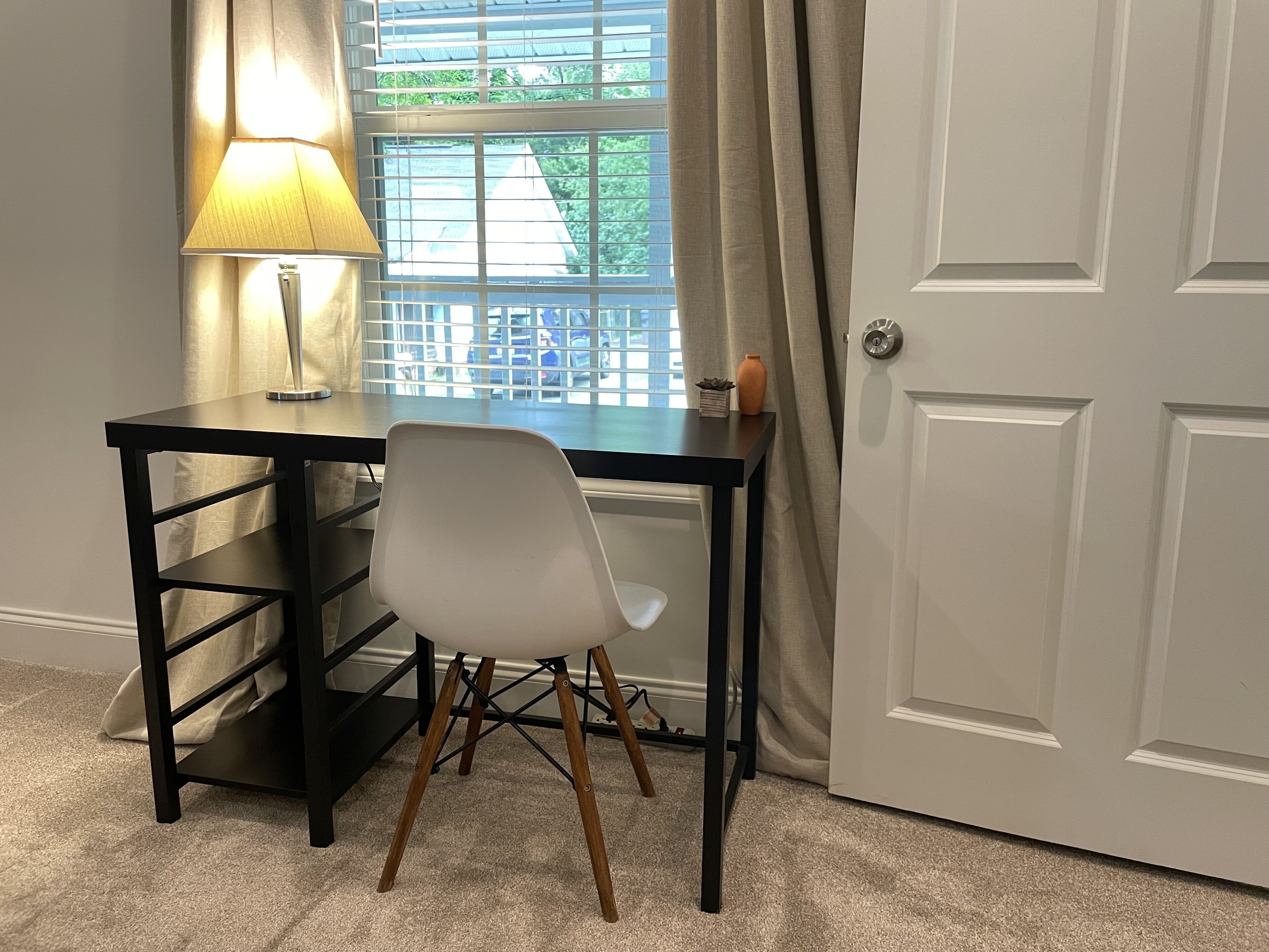Ein Zimmer mit Schreibtisch, Stuhl, Lampe und einer Tür.