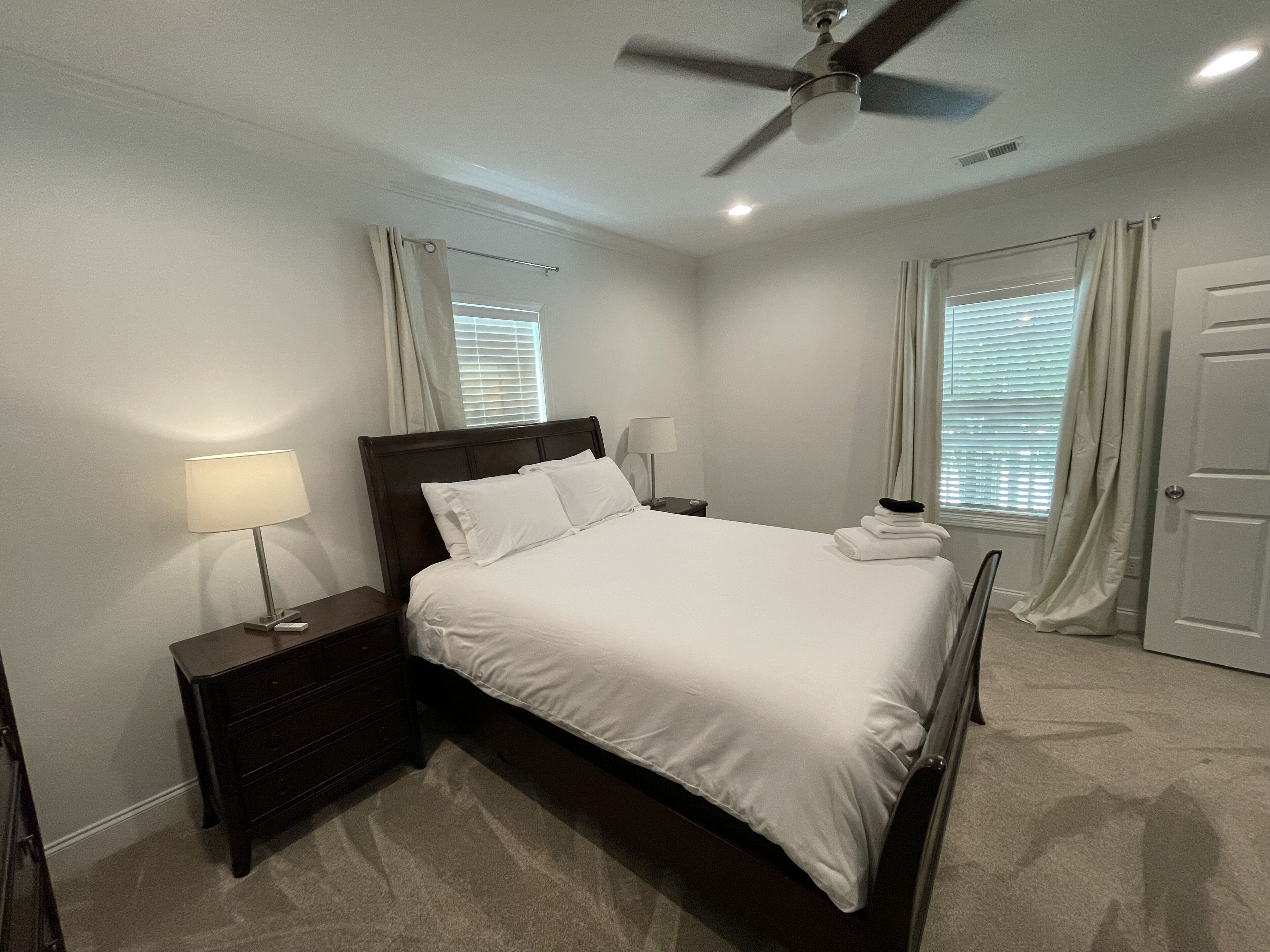 A bedroom with a bed, nightstands, a ceiling fan, and a door.