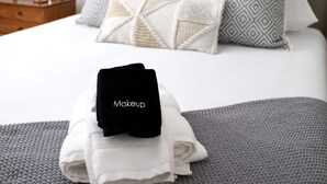 Ein ordentlich bezogenes Bett mit gemusterten Kissen, einer grauen Decke und einer schwarzen Kosmetiktasche mit der Aufschrift "Makeup" auf einer grau strukturierten Oberfläche.