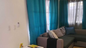 A living room with a sofa, a small table with a chair, and a window with curtains.