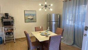 A dining area with a table, chairs, a ceiling light fixture, a refrigerator, and a microwave on a shelf.