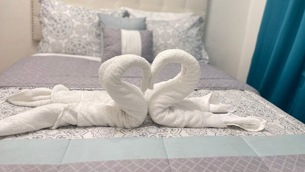 A bed with a patterned bedspread and pillows, a headboard, and a blue curtain.