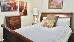 Een slaapkamer met een houten bed, een nachtkastje met een lamp, een dressoir en twee abstracte schilderijen aan de muur.