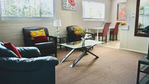 Een woonkamer met een bank, twee fauteuils, een glazen salontafel, en een eethoek met een tafel en stoelen.