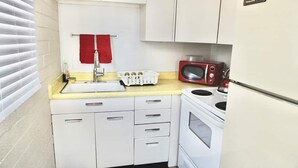 Een kleine keuken met witte kastjes, een spoelbak, een rode magnetron en een fornuis.