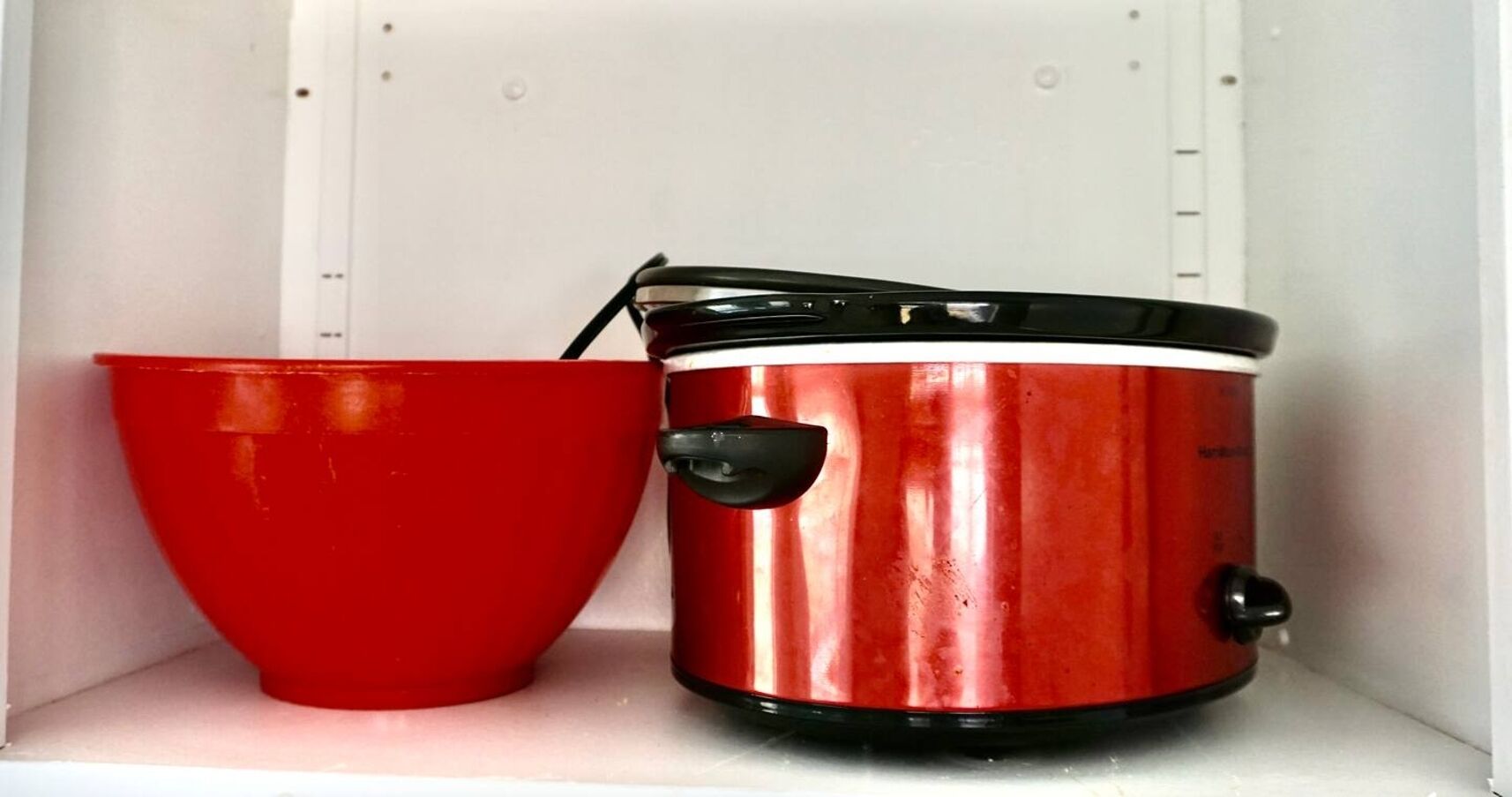 A red pot and a red bowl on a white shelf.