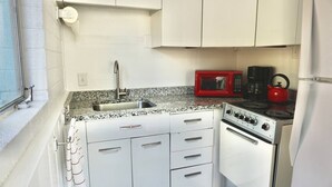 Une cuisine de taille réduite, dotée d’un plan de travail en granit, d’un four à micro-ondes rouge, d’une cuisinière et d’un évier.