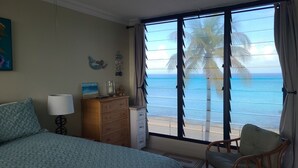 A bedroom with a large window, a bed, a dresser, and a chair.
