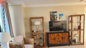 A living room with wicker furniture, a flat-screen TV, and decorative items on shelves.