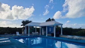 A clear blue swimming pool with lounge chairs and a covered seating area.