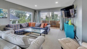 Una sala de estar con un sofá modular, una mesa de centro de vidrio y un televisor montado en la pared.