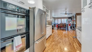 Una cocina moderna con electrodomésticos de acero inoxidable, piso de madera y un comedor con una silla roja.
