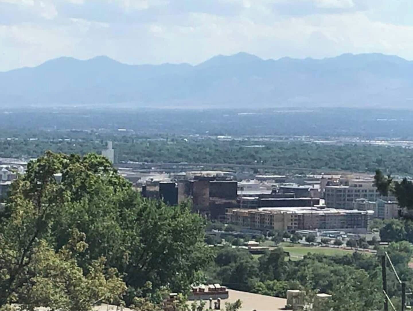 Un paisaje urbano con edificios, árboles y montañas al fondo.