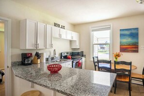 Una cocina con armarios blancos, encimera de granito, una cesta tejida roja y un cuadro en la pared.