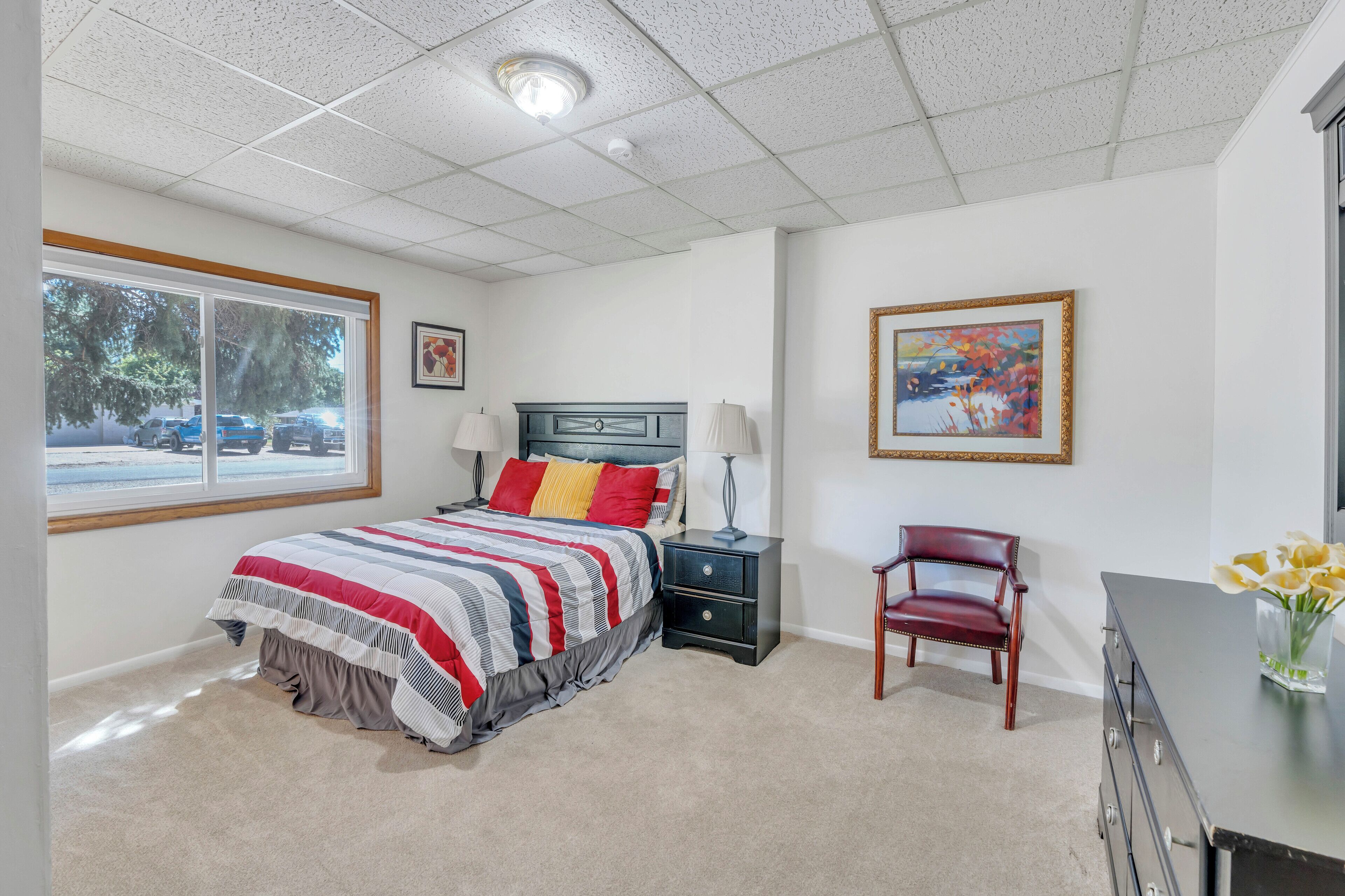 A bedroom with a bed, nightstand, chair, dresser, and a painting on the wall.