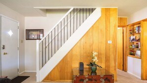 A staircase with wooden paneling, a glass coffee table with a vase of flowers, and a bookshelf with various items. - Heritage House -Great Location, Skiing, Walk to Restaurants, Sports Fields, Train.  Large rooms (Heber City)
