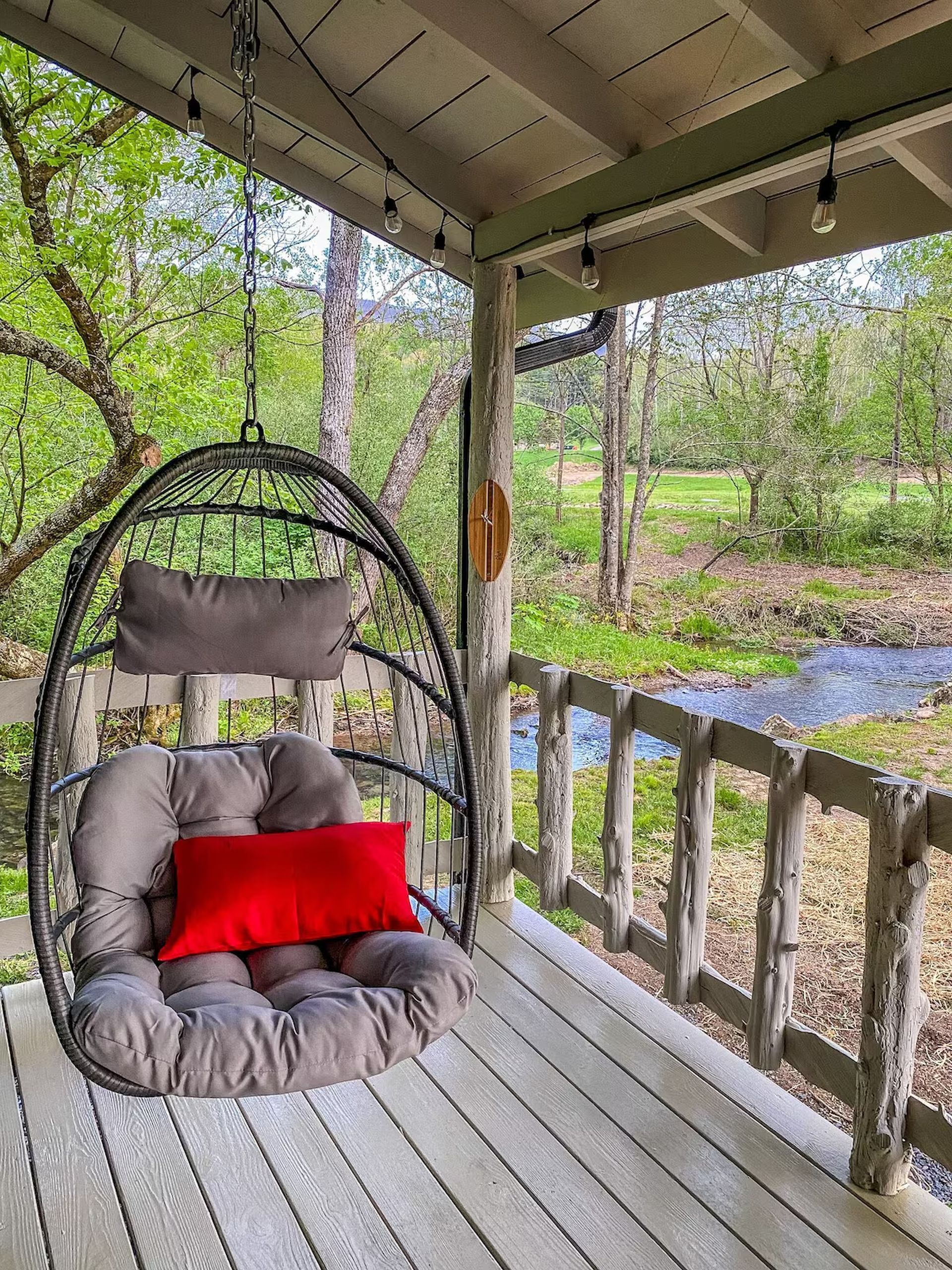 A wooden porch with a hanging chair and a view of a natural landscape.