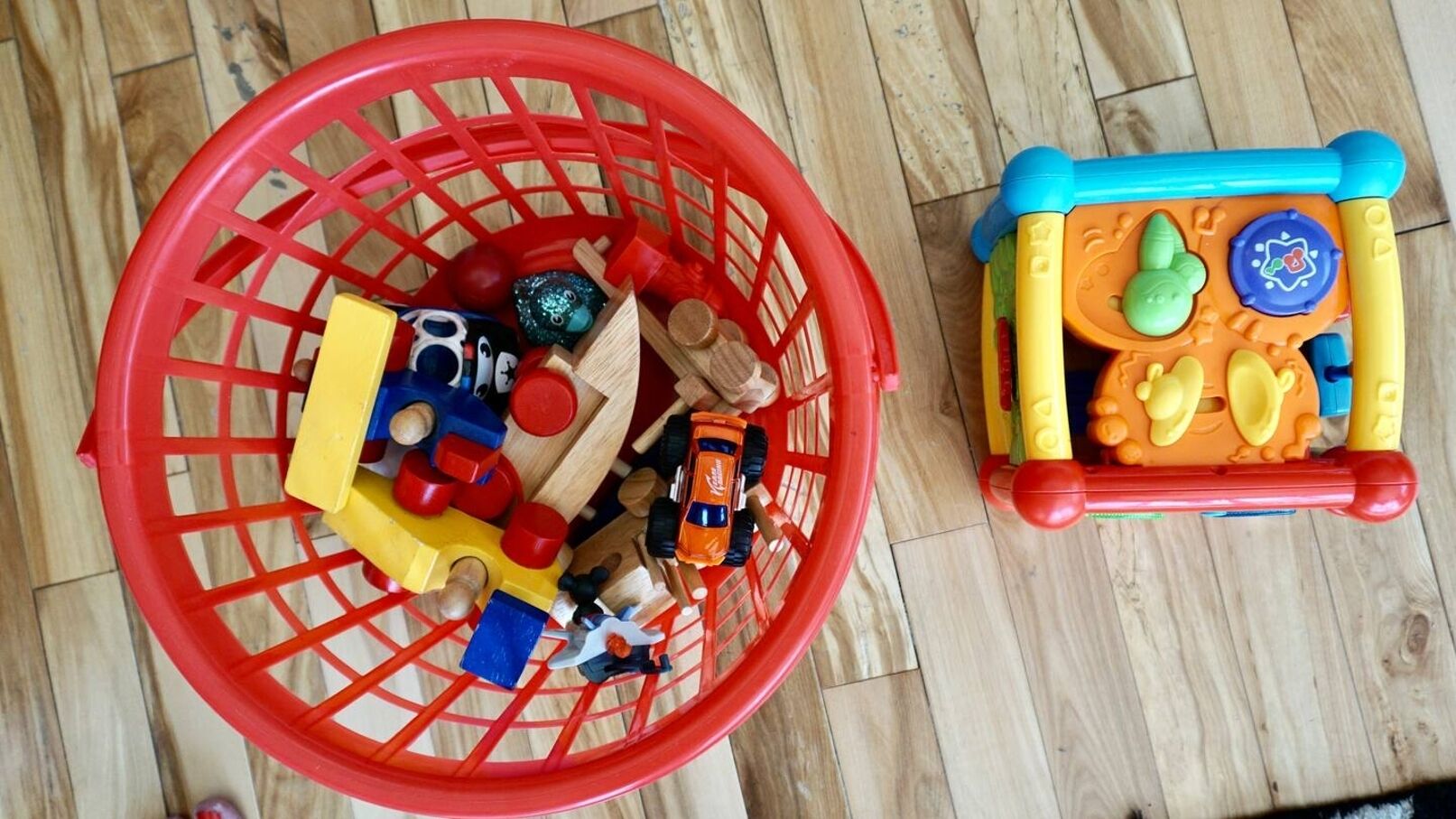 Un panier en plastique rouge rempli de différents jouets et une petite voiture jouet.