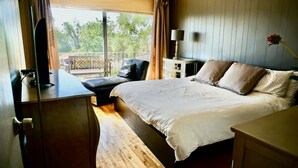 Ein Schlafzimmer mit Bett, Schreibtisch, Stuhl und einem Balkon mit Blick auf Bäume.