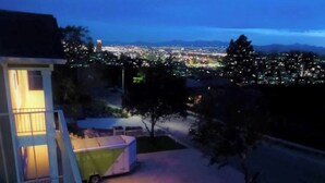 Ein Wohngebiet im Abenddämmerung mit einem Haus, einem abgestellten Wohnmobil und Blick auf eine Stadtkulisse im Hintergrund.